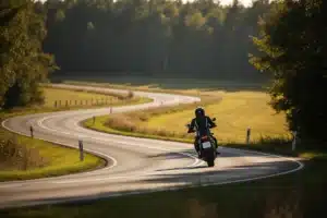 Motard de dos sur une route de campagne sinueuse, illustrant l'assurance moto au kilometre pour les petits rouleurs