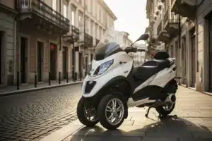 Piaggio MP3 blanc trois roues garé sur une rue pavée européenne, vue avant trois quarts montrant les deux roues avant