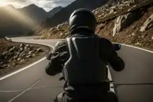Motard portant un gilet airbag moto sur route de montagne sinueuse, protection dorsale et thorax visible de dos