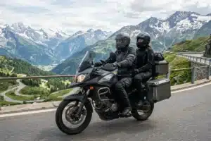Deux motards équipés sur une GT avec valises latérales, route de montagne en arrière-plan