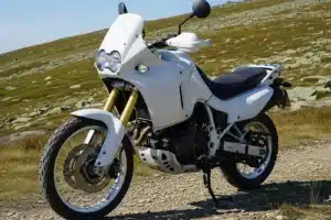 Moto trail aventure de couleur blanche à l'arrêt sur une piste de montagne caillouteuse