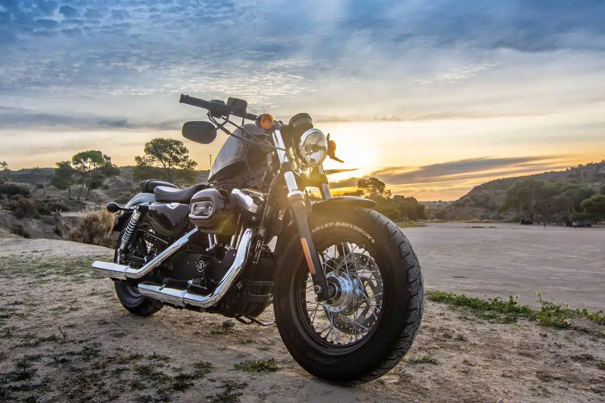 Moto cruiser garée au coucher du soleil Moto cruiser noire de type Harley-Davidson garée sur un terrain au coucher du soleil, vue de face trois quarts