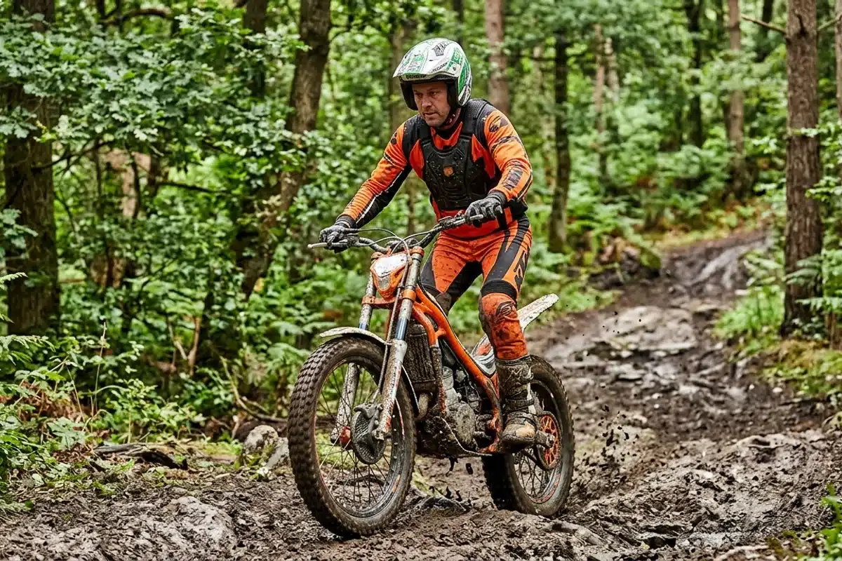 Moto de trial en forêt avec équipement FFM Motard en tenue de trial sur moto orange dans la boue en forêt