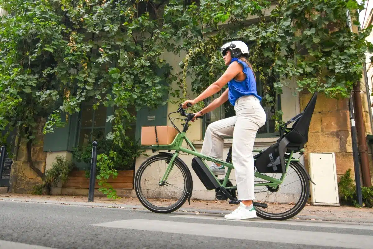 Femme à l'arrêt sur un vélo cargo électrique équipé d'un siège enfant dans une rue urbaine