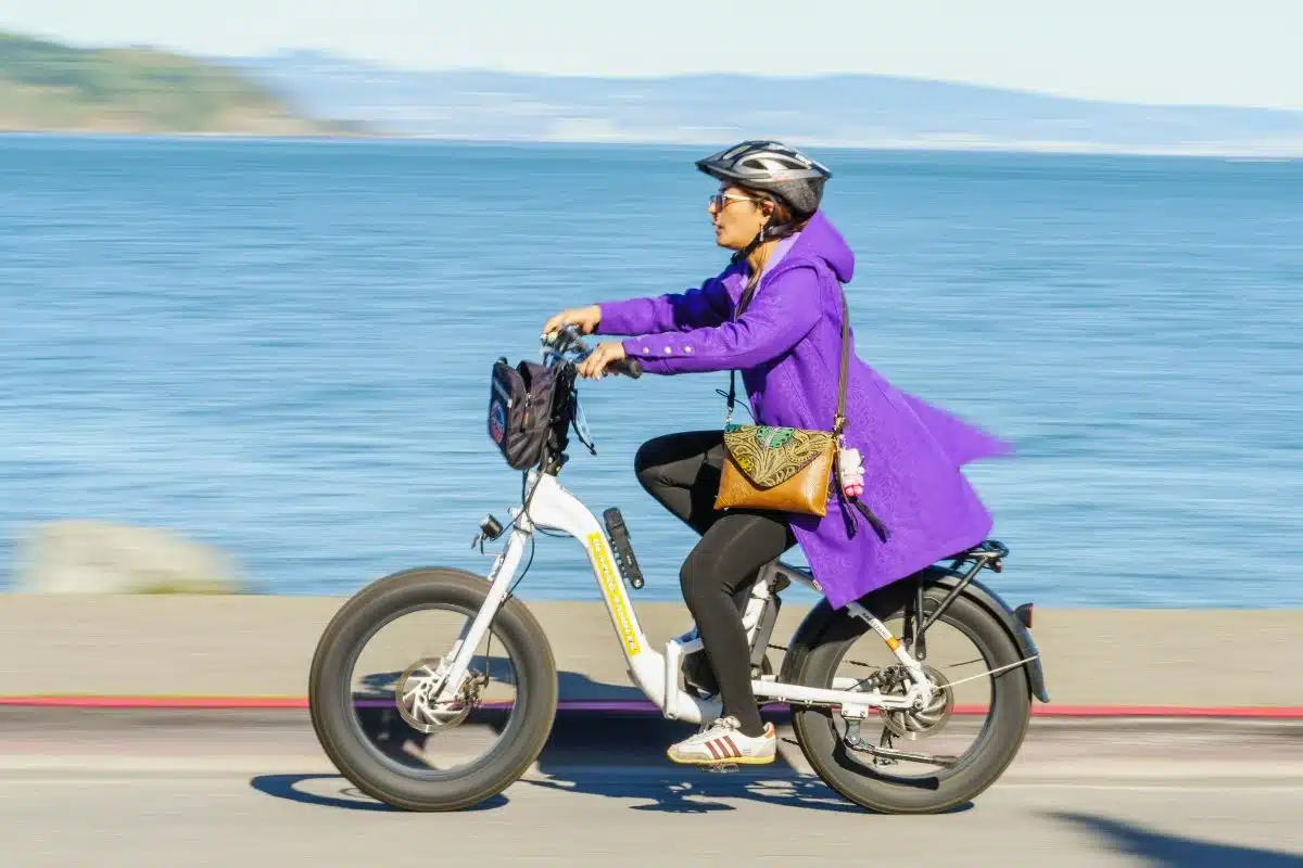 Cycliste casquée roulant à vive allure sur un vélo électrique à gros pneus en bord de mer