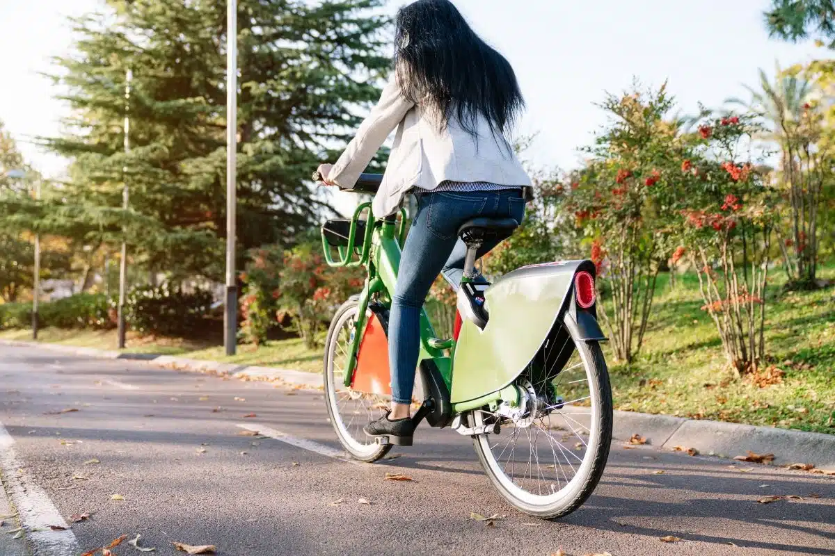 Femme circulant à vélo électrique sur une piste cyclable urbaine en automne