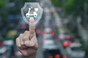 Icône bouclier contenant un scooter, symbole de l'assurance d'un deux-roues, au-dessus d'un trafic urbain
