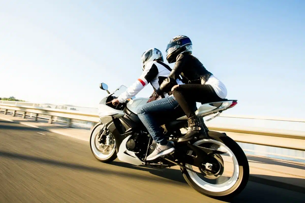 Un motard et son passager roulent à moto sur une voie rapide par temps dégagé